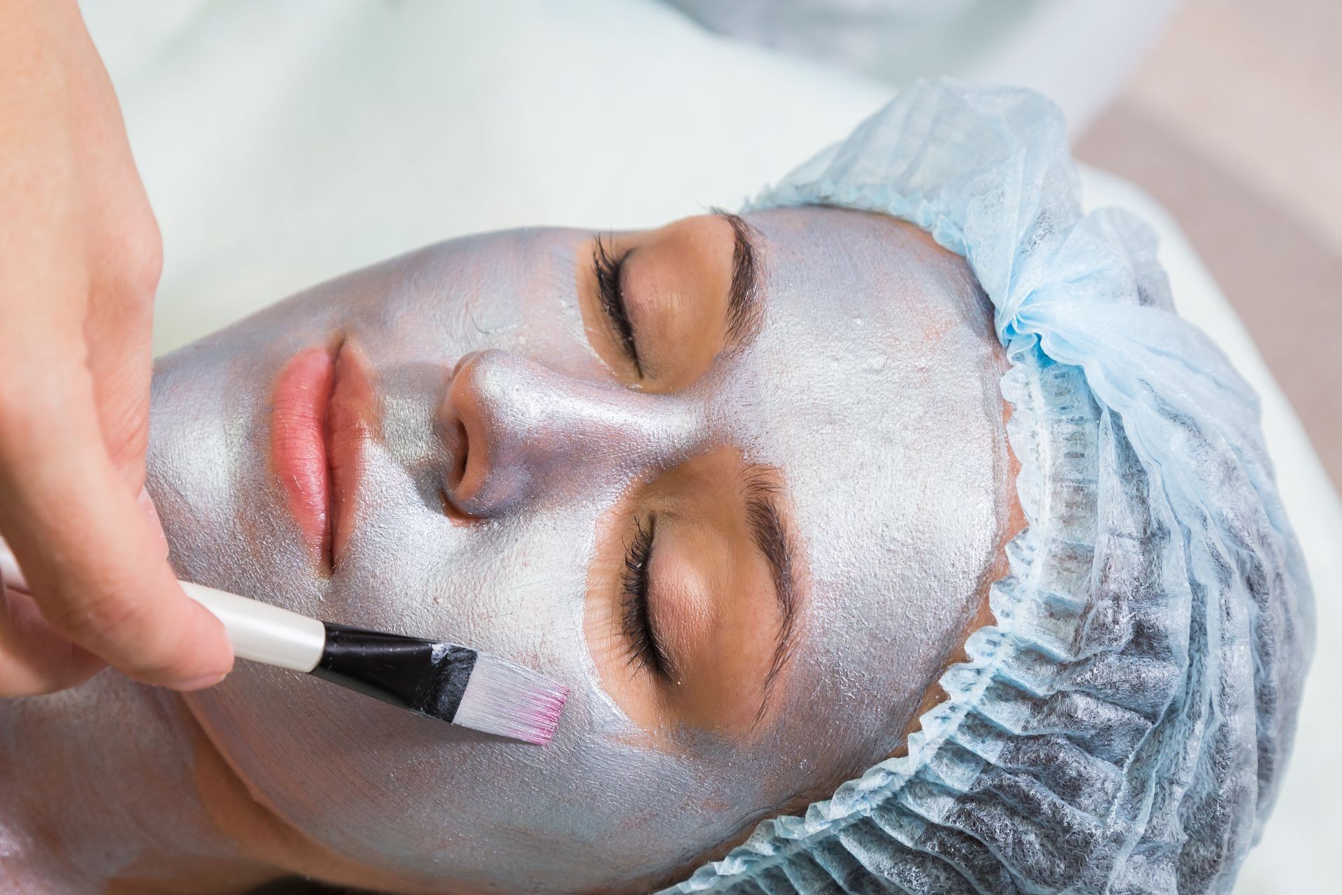 Young woman at spa procedures applying mask. Therapist applying a face mask to the face of a beautiful young  woman using a cosmetic brush.Cosmetology,facial, beauty - The concept of facial skin care.